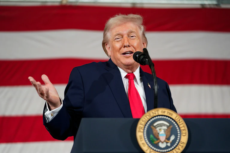 Donald Trump holds his hand out and smiles while speaking behind a lectern