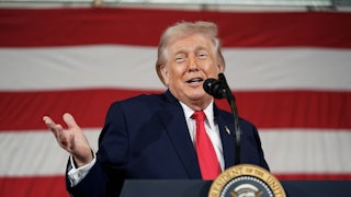 Donald Trump holds his hand out and smiles while speaking behind a lectern