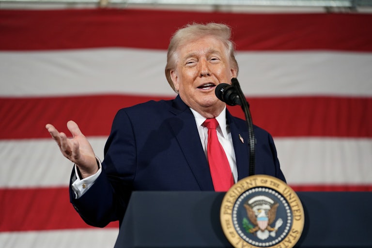 Donald Trump holds his hand out and smiles while speaking behind a lectern