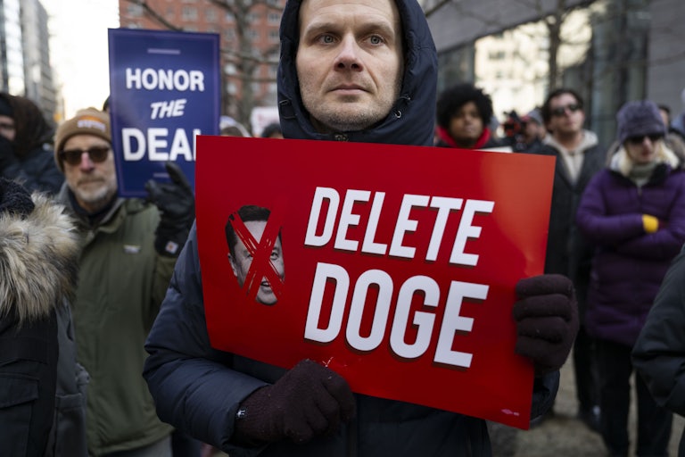 A person holds up a sign that says, "Delete DOGE" during an anti-Trump and anti-Elon Musk protest
