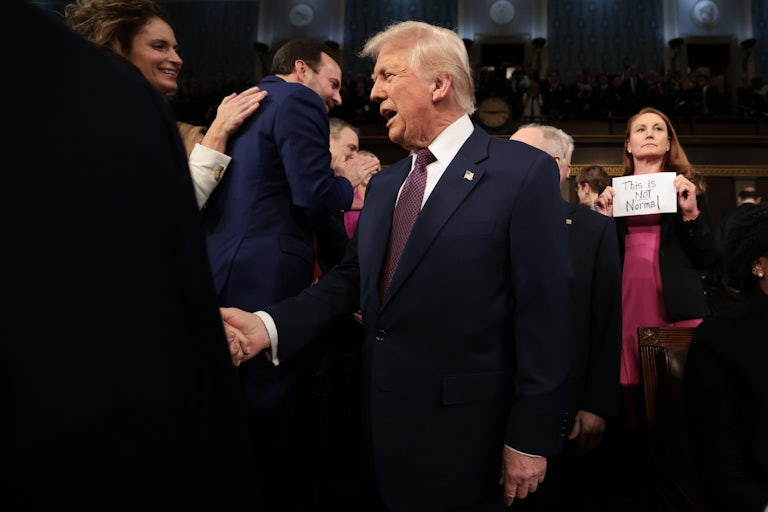 Representative Melanie Stansbury holds a piece of paper "THIS IS NOT NORMAL" behind Donald Trump as he greets other members of Congress in the Capitol.