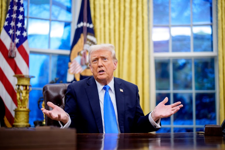 Donald Trump sits at the Resolute Desk in the Oval Office and splays both palms outward as if in confusion.