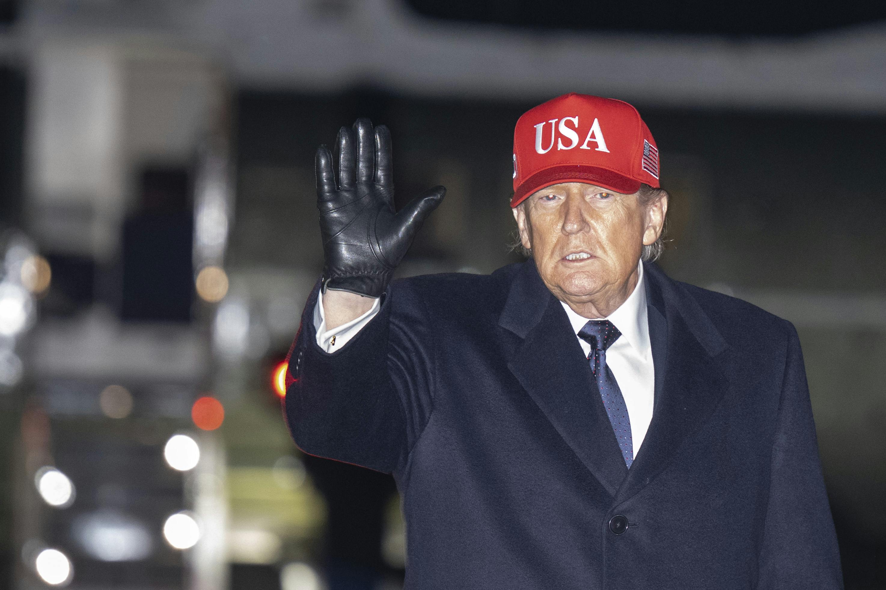 Donald Trump waves while wearing a USA cap.