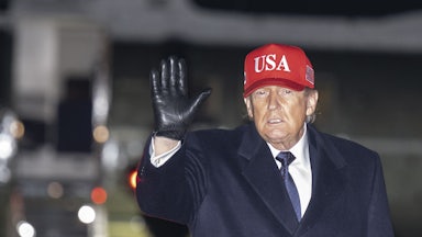 Donald Trump waves while wearing a USA cap.
