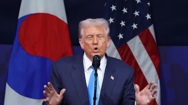Donald Trump raises both hands while speaking at a podium during a summit in South Korea