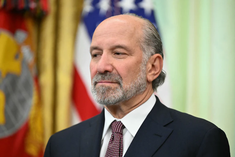 Commerce Secretary Howard Lutnick smiles slightly and stares off into space