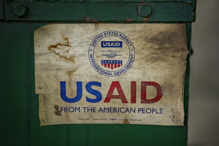 A tattered sign reads "USAID FROM THE AMERICAN PEOPLE"