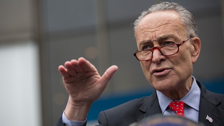 Senator Chuck Schumer extends his hand, gesticulating at a press conference.