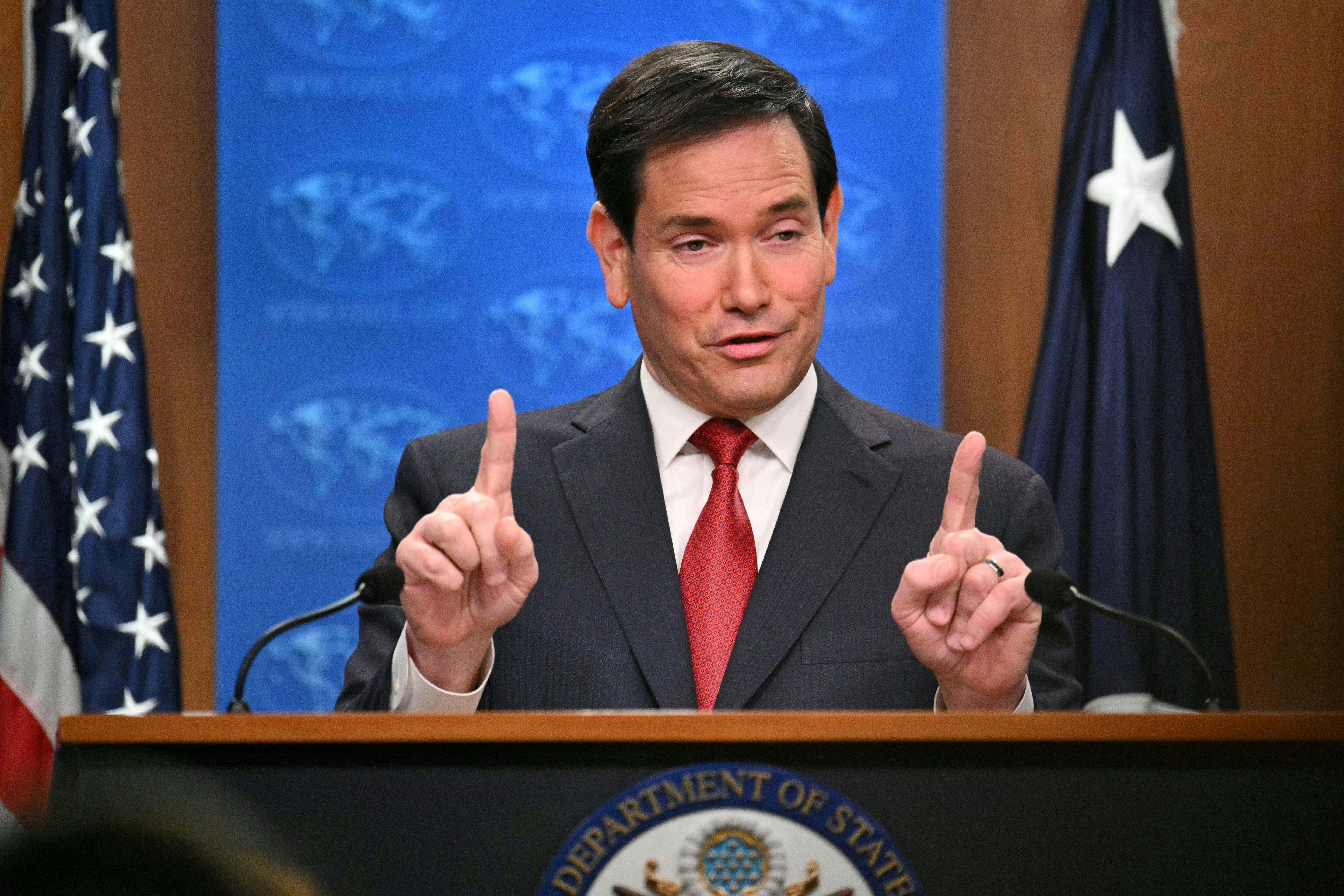 Secretary of State Marco Rubio raises both index fingers while speaking at a podium