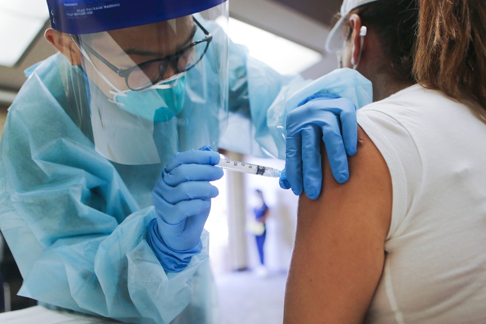 A nurse administers a flu shot at a free clinic, wearing protective gear against Covid-19.