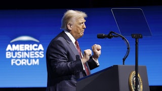 Donald Trump raises his fists and dances while standing at a podium on stage at the American Business Forum