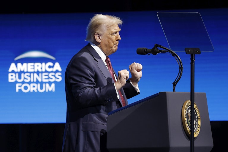Donald Trump raises his fists and dances while standing at a podium on stage at the American Business Forum