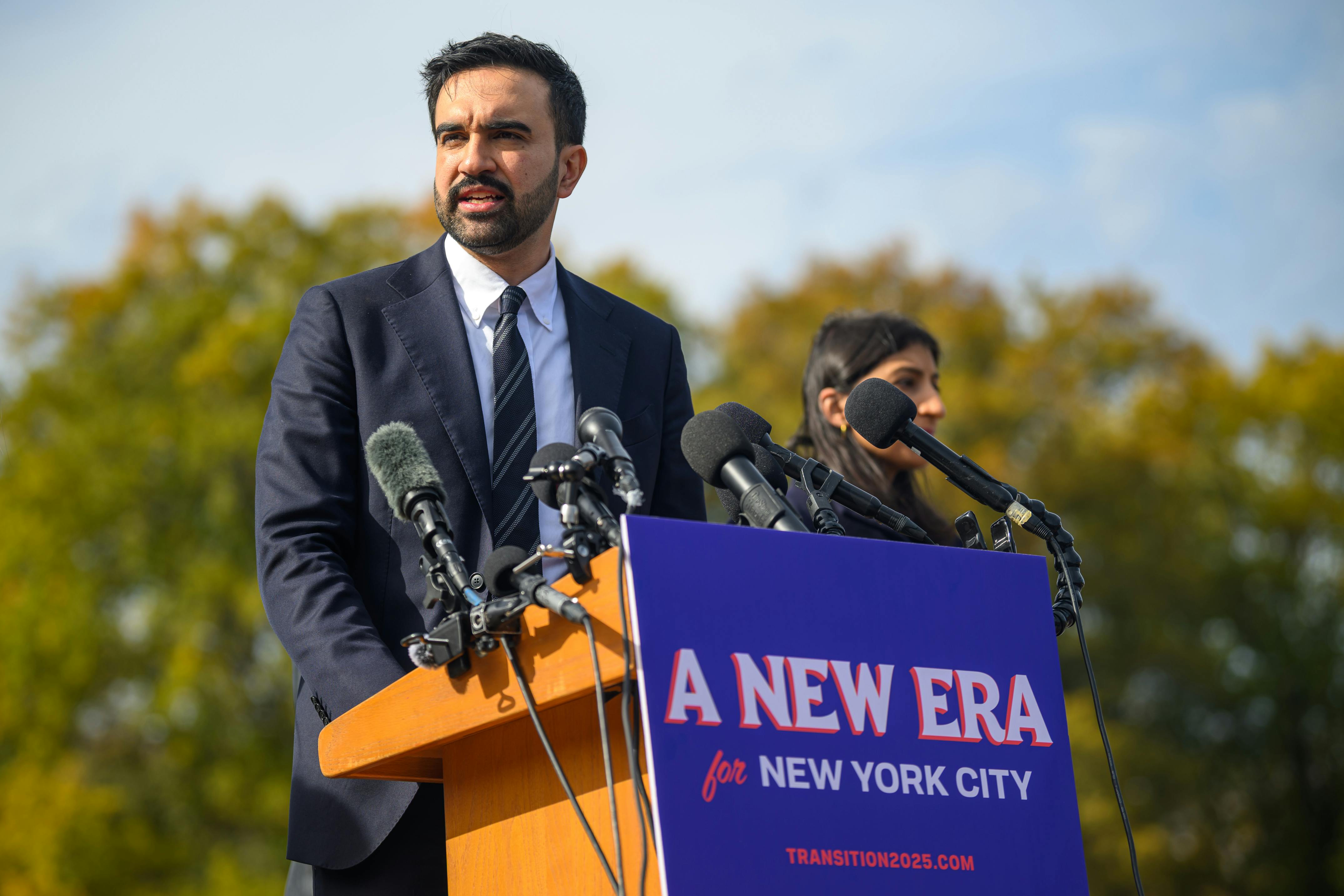Zohran Mamdani speaks at a lectern with a sign that reads "A New Era for New York City."
