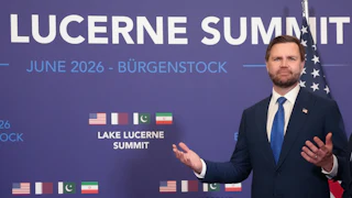 JD Vance stands in front a blue backdrop mentioning the Lucerne Summit on June 2016 in Switzerland with the flags of the U.S., Qatar, Pakistan, and Iran on the backdrop.