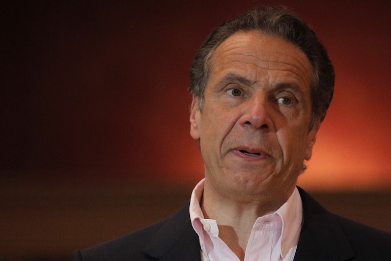 New York Governor Andrew Cuomo stands against a backdrop of red light 