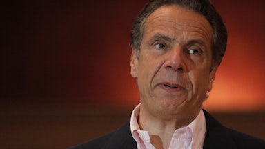 New York Governor Andrew Cuomo stands against a backdrop of red light