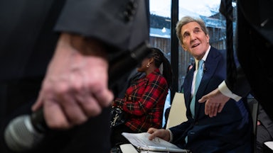 John Kerry looks up, smiling, while paging through a binder.