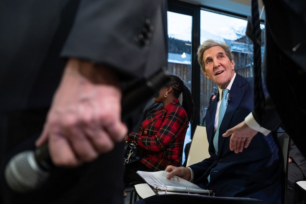 John Kerry looks up, smiling, while paging through a binder.