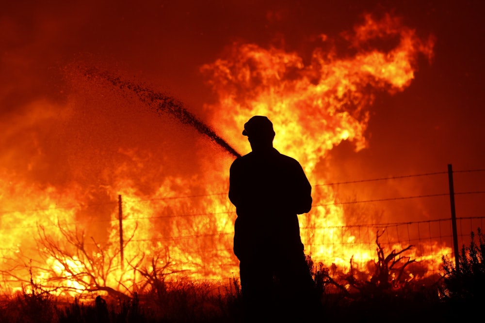 A utility worker uses a hose to extinguish a fire near power poles as the Dixie Fire moves near Janesville, California.