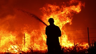 A utility worker uses a hose to extinguish a fire near power poles as the Dixie Fire moves near Janesville, California.