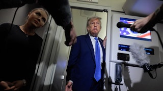Donald Trump shrugs as he and Karoline Leavitt stand in front of reporters aboard Air Force One.