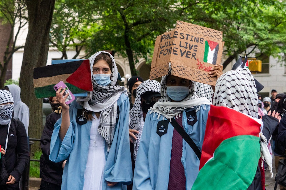 Wearing keffiyehs and graduation gowns, Columbia students hold a sign saying "Palestine Will Love Forever" at their graduation
