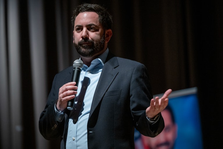 Representative Mike Lawler shrugs and holds a microphone while standing on stage at a town hall