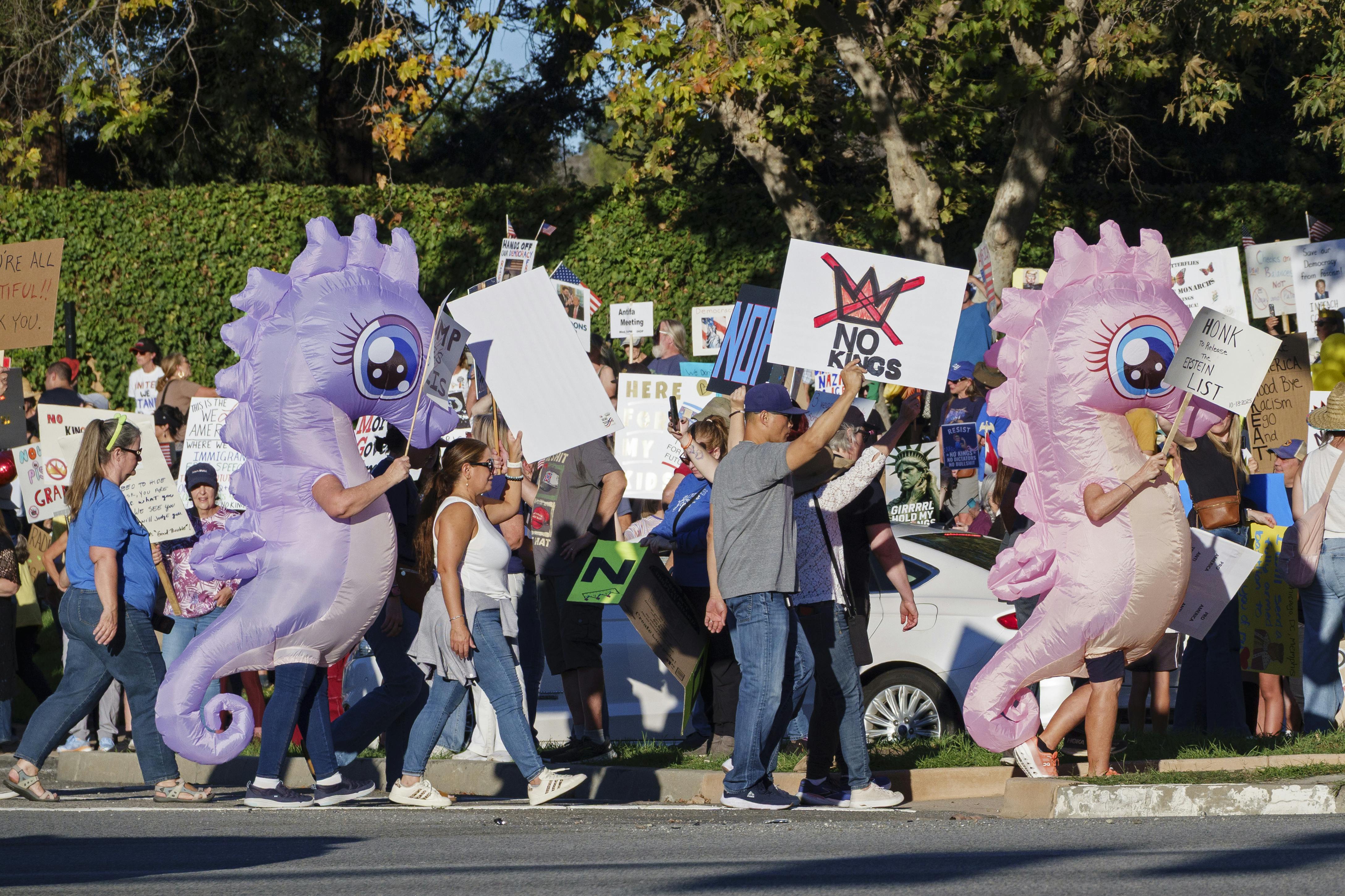 People, including two in inflatable seahorse costumes, march and hold signs during the No Kings protest