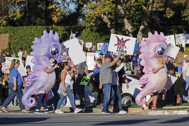People, including two in inflatable seahorse costumes, march and hold signs during the No Kings protest