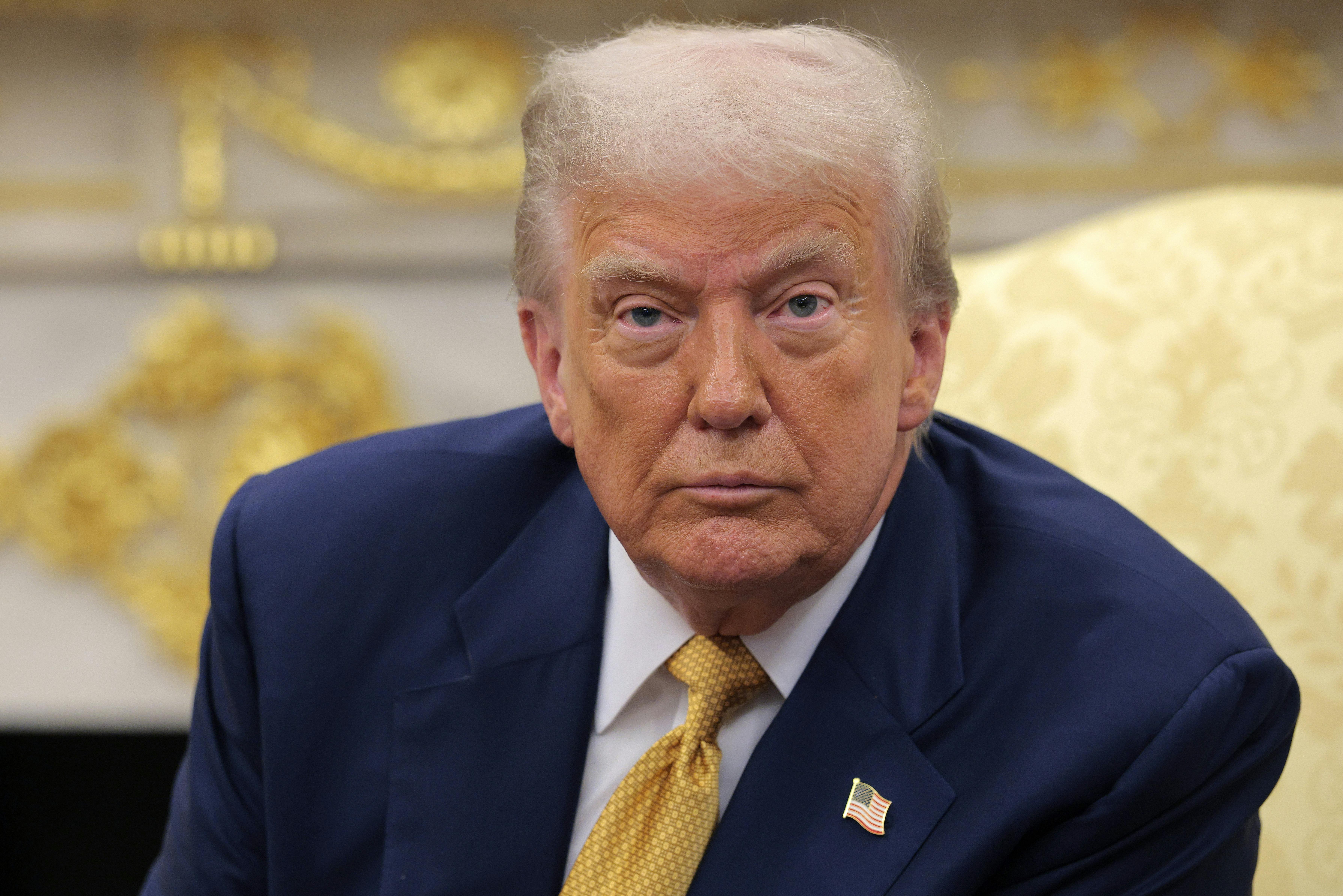 Donald Trump sits in the Oval Office and stares ahead with bloodshot eyes