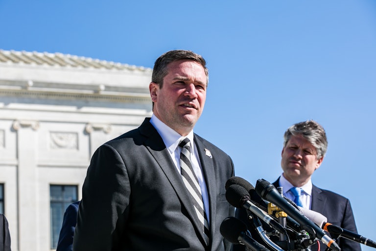 Missouri Attorney General Andrew Bailey stands outside at a lectern with several mics