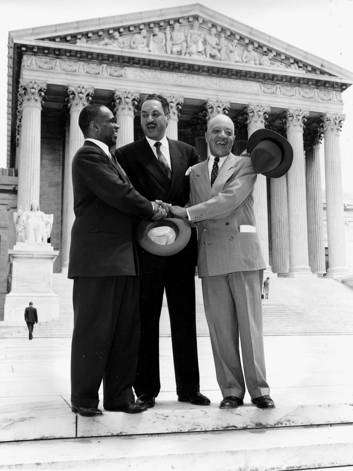 A photo from May 17, 1954 showing George E.C. Hayes, Thurgood Marshall, and James M. Nabrit joining hands after the ruling on Brown v. Board of Education that school segregation is unconstitutional.