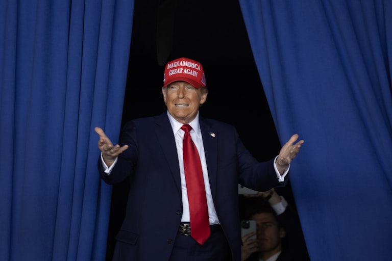 Donald Trump wears a MAGA hat and holds his arms out in front of himself