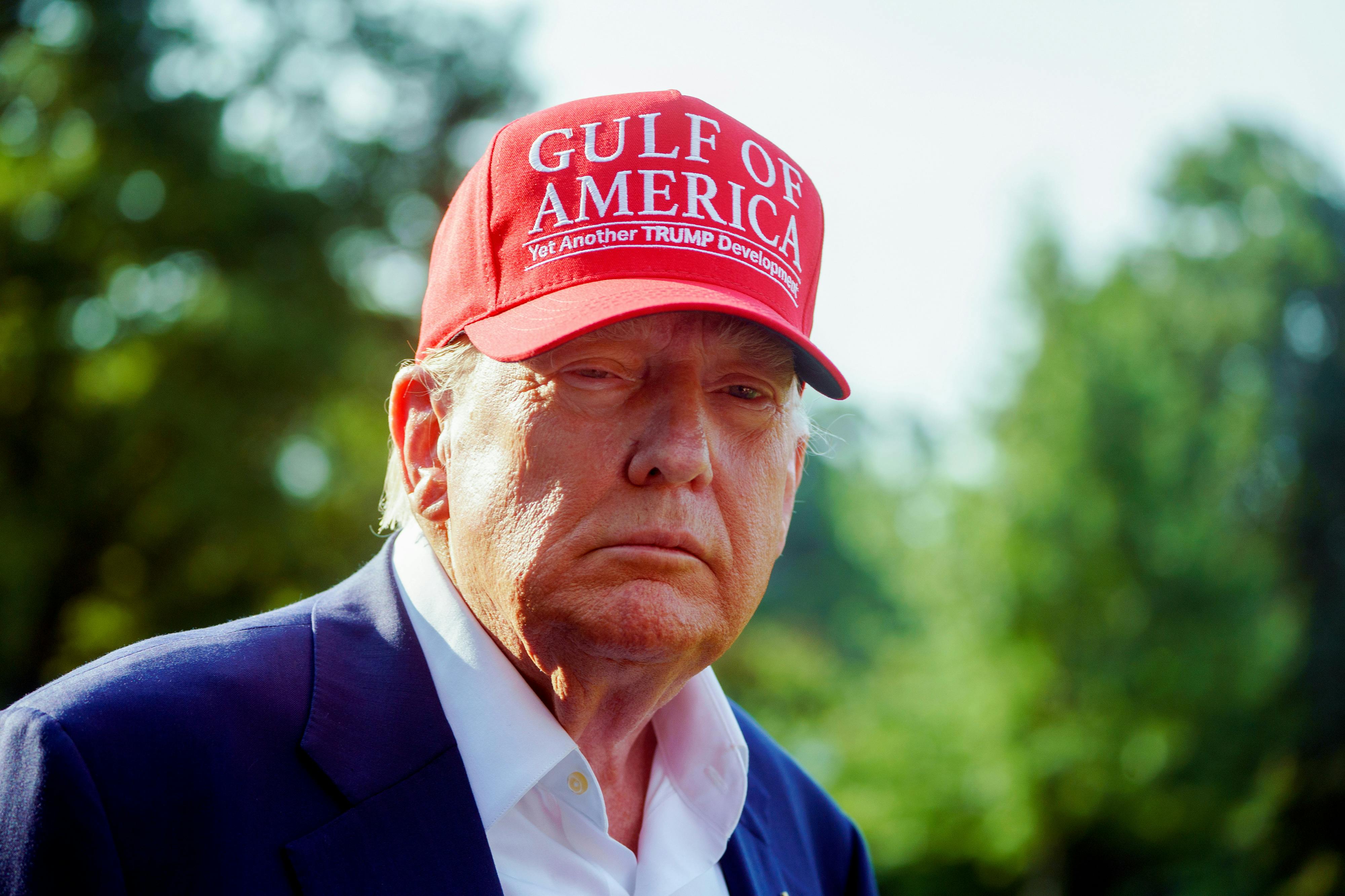 Donald Trump squints his eyes while wearing a Gulf of America cap in the sun.