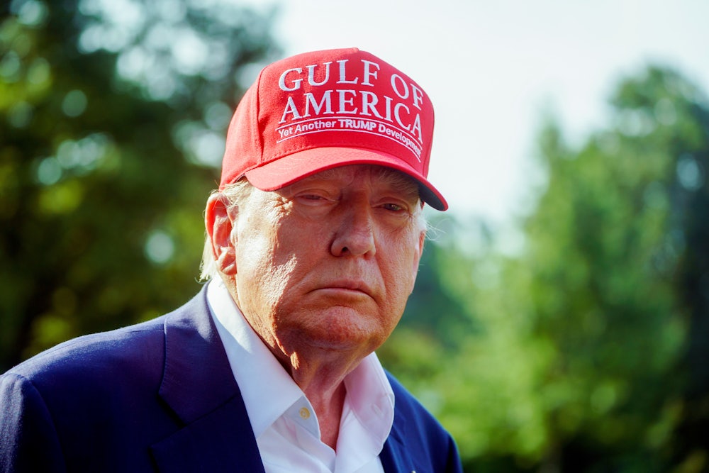Donald Trump squints his eyes while wearing a Gulf of America cap in the sun.