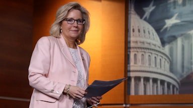 A smirking Liz Cheney carries papers through the U.S. Capitol.