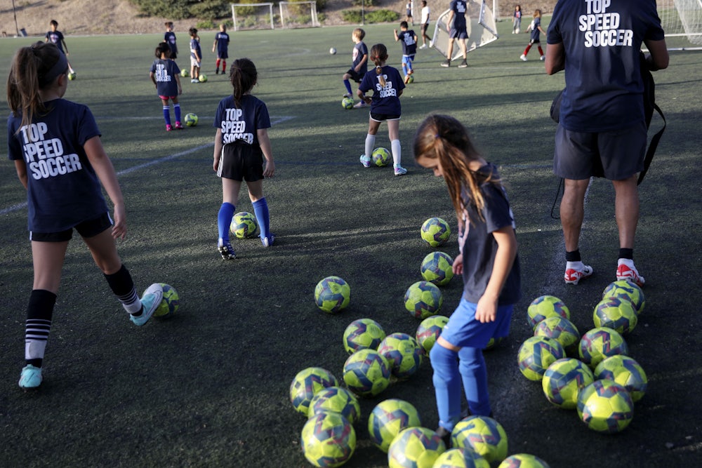Children kick soccer balls on artificial turf.