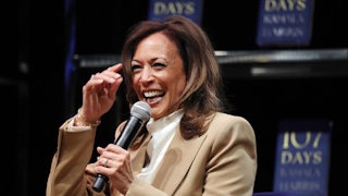 Kamala Harris laughs while she speaks on a mic. Her book 107 Days is in the background.
