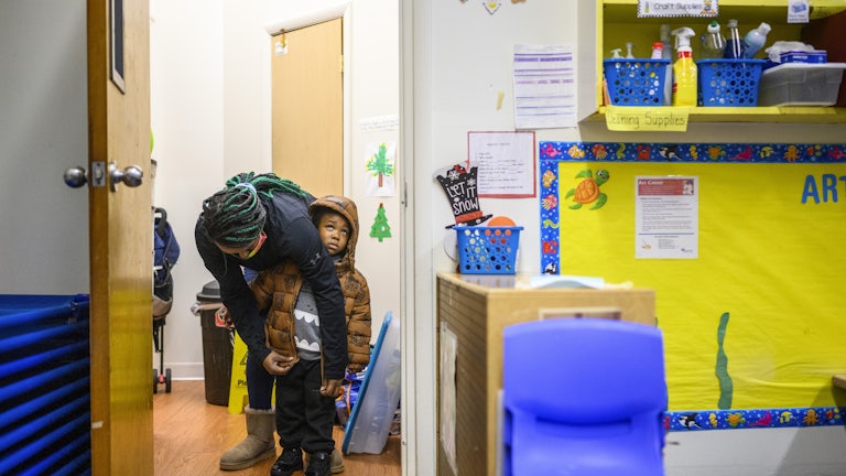 A teacher zips up the coat of a 3-year-old