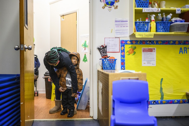 A teacher zips up the coat of a 3-year-old