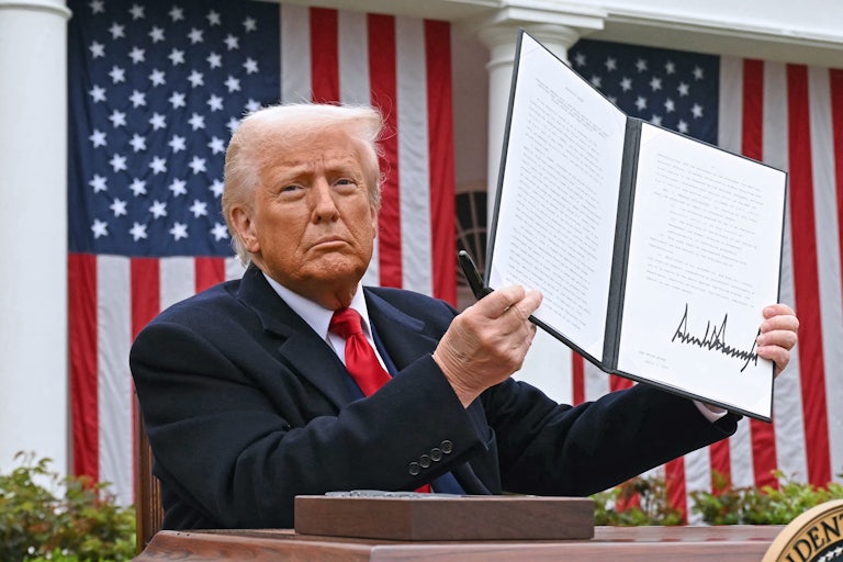 Donald Trump holds up a signed executive order while sitting at a table in the White House Rose Garden
