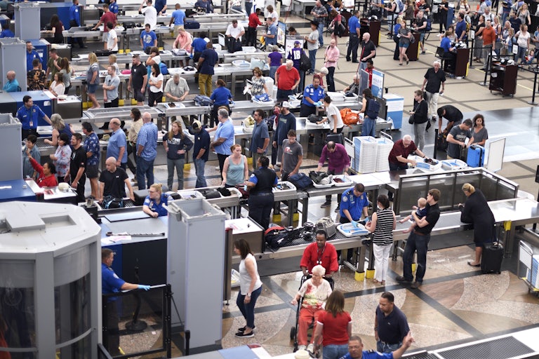 Lines of airplane passengers proceed through a TSA security checkpoint at an airport.