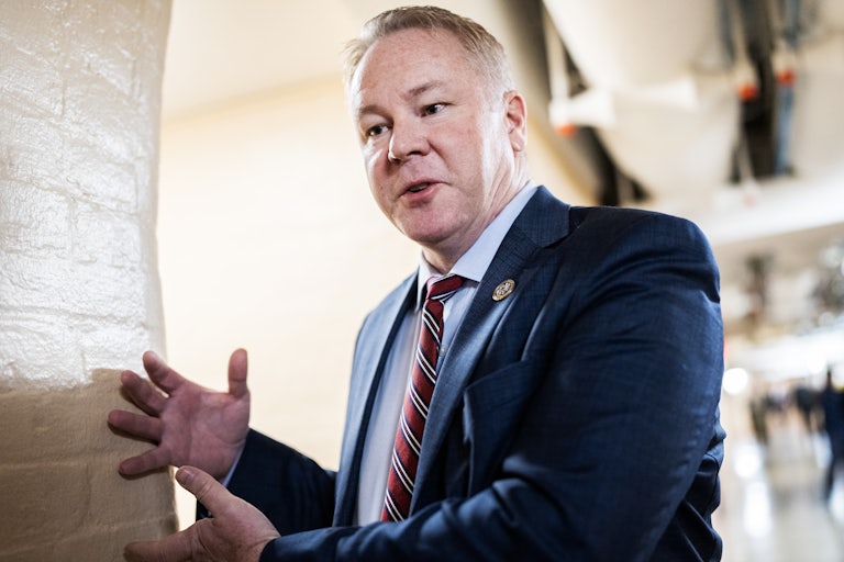 Representative Warren Davidson, looking downward, speaks and makes a weird hand gesture very close to a wall