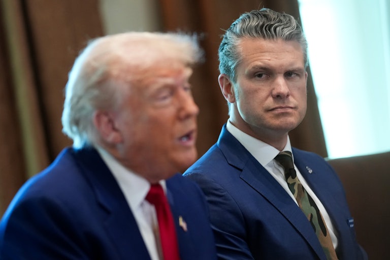 Defense Secretary Pete Hegseth watches as Donald Trump, seated beside him in the White House, speaks.