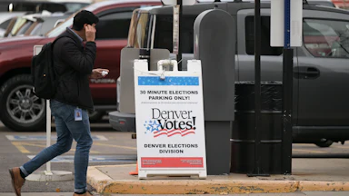 A man walks by an election sign that reads "Denver Votes!"