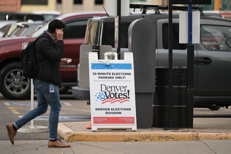 A man walks by an election sign that reads "Denver Votes!"