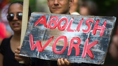 A May Day demonstrator holds a sign that reads "Abolish Work"