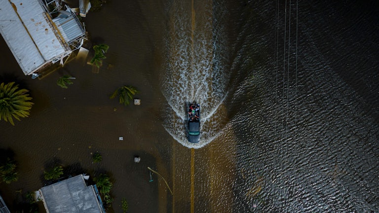 An aerial view shows a car driving through water.