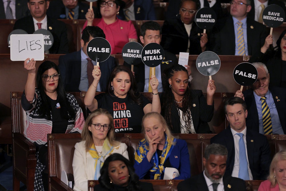 Rep. Rashida Tlaib joins fellow Democrats in holding up signs to protest against President Donald Trump as he addresses a joint session of Congress.