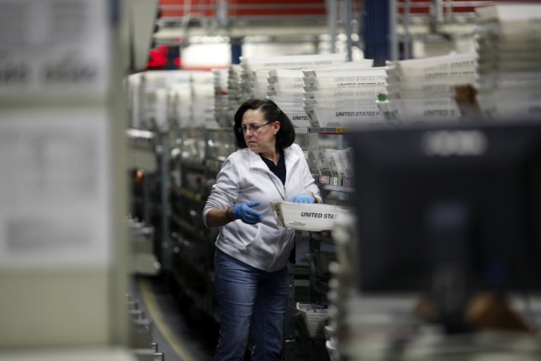 A USPS employee carries a bin of mail at a processing center